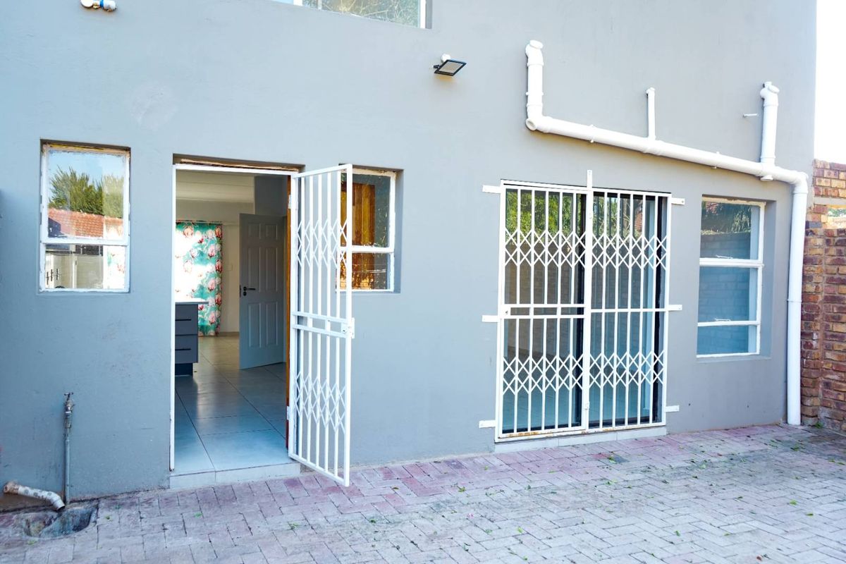 Rear exterior view of the apartment featuring paved patio area, security gates, and access to the interior living space.