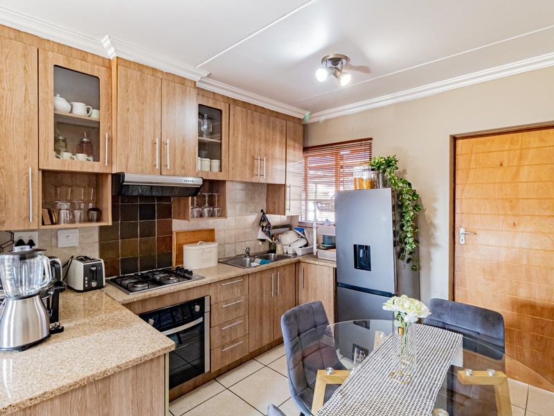 A functional kitchen featuring wood-look laminate cabinetry, granite countertops, a gas hob, built-in oven, and tiled flooring with a neutral backsplash.