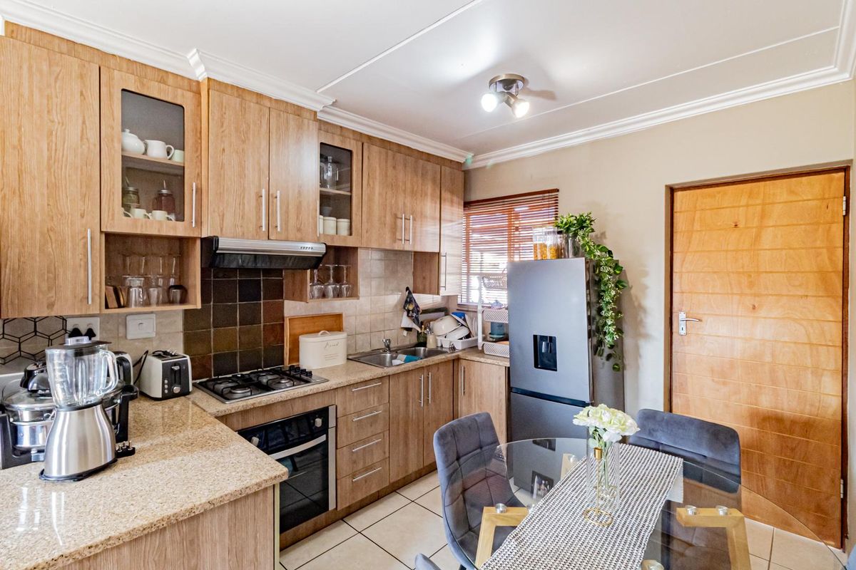 A functional kitchen featuring wood-look laminate cabinetry, granite countertops, a gas hob, built-in oven, and tiled flooring with a neutral backsplash.