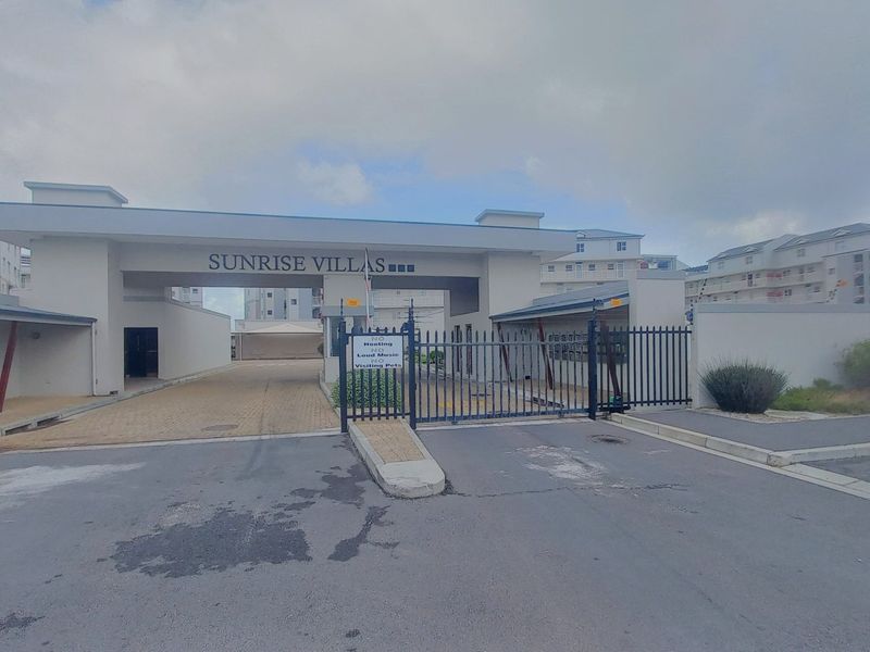 The main entrance to Sunrise Villas apartment complex, featuring a secure gated access point, paved driveway, and perimeter walling.