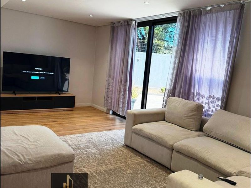 A bright and modern living room featuring hardwood flooring, recessed downlighting, and large sliding glass doors that provide access to the outdoor area.