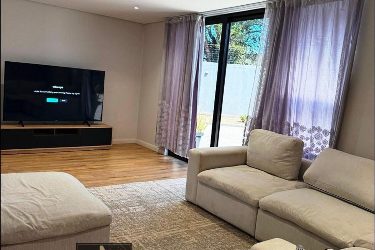 A bright and modern living room featuring hardwood flooring, recessed downlighting, and large sliding glass doors that provide access to the outdoor area.