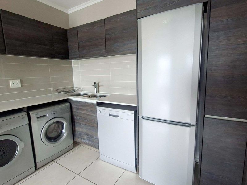 Modern kitchen featuring dark wood-look cabinetry, light tiled backsplash, and dedicated spaces for laundry appliances and a refrigerator.