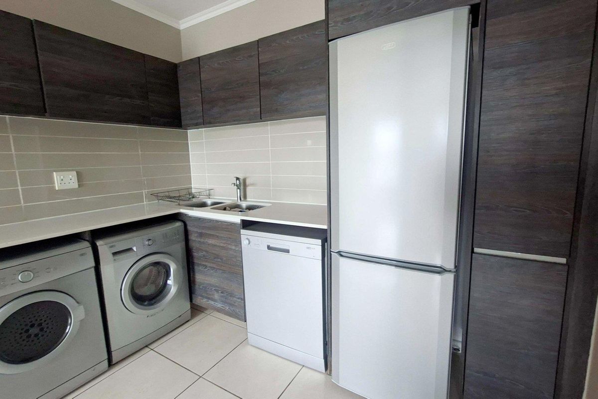 Modern kitchen featuring dark wood-look cabinetry, light tiled backsplash, and dedicated spaces for laundry appliances and a refrigerator.