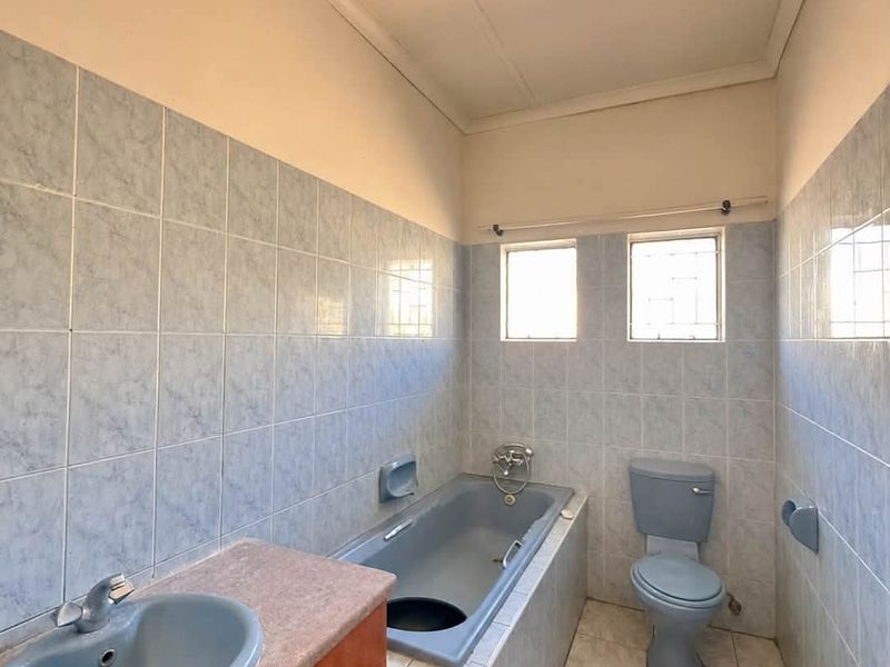 A dated bathroom featuring blue sanitary ware, tiled walls and floors, and a built-in vanity unit, offering potential for a modern renovation.