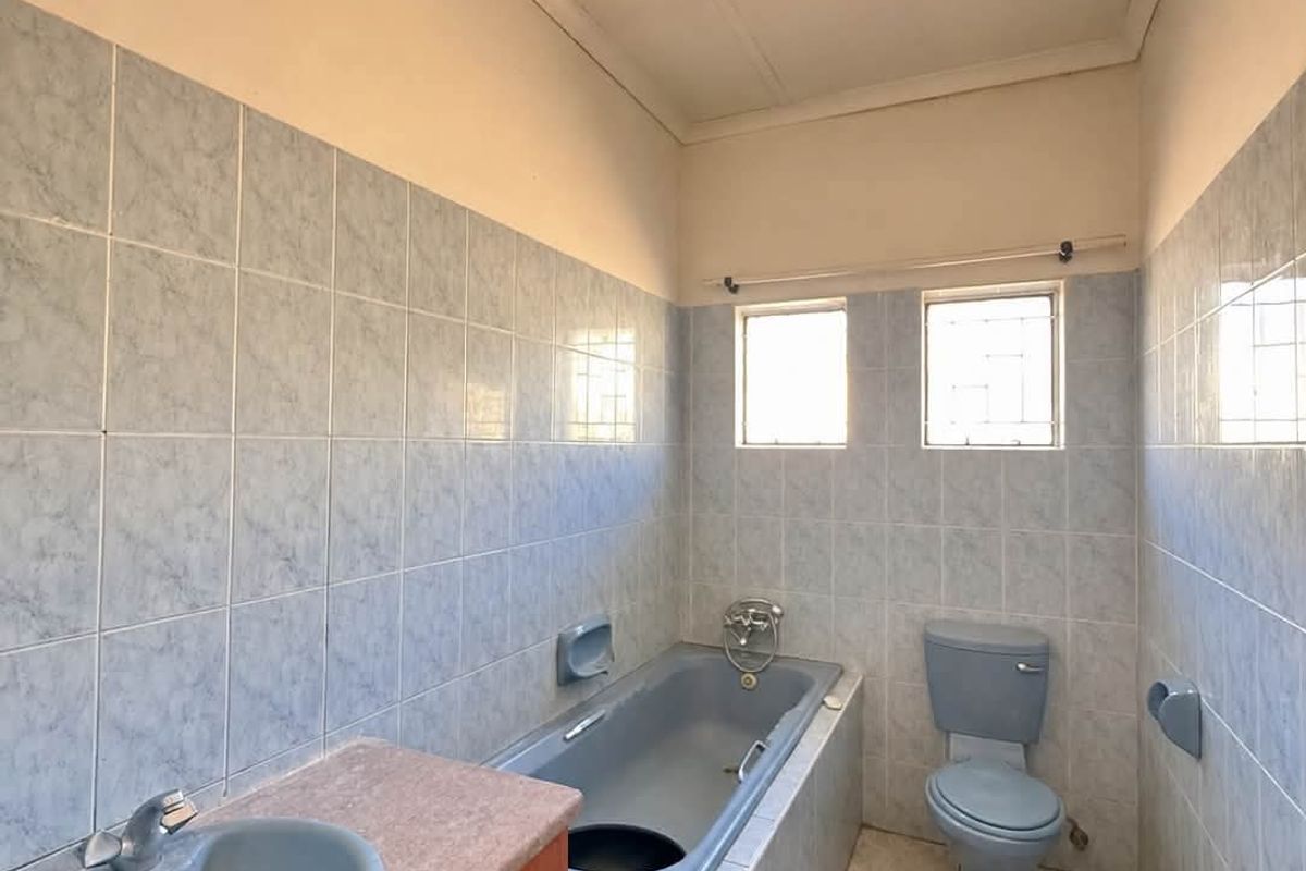 A dated bathroom featuring blue sanitary ware, tiled walls and floors, and a built-in vanity unit, offering potential for a modern renovation.