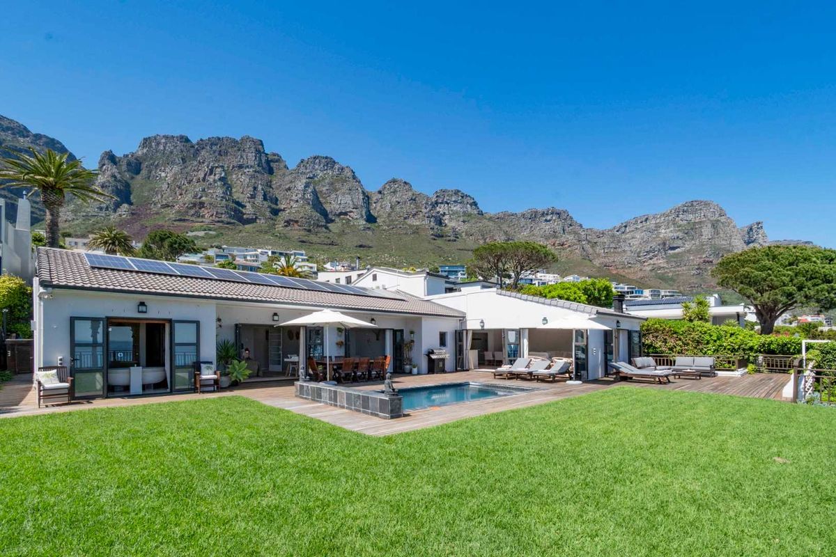 Spacious rear exterior featuring a swimming pool, timber decking, and bi-fold doors, set against a scenic mountain backdrop.