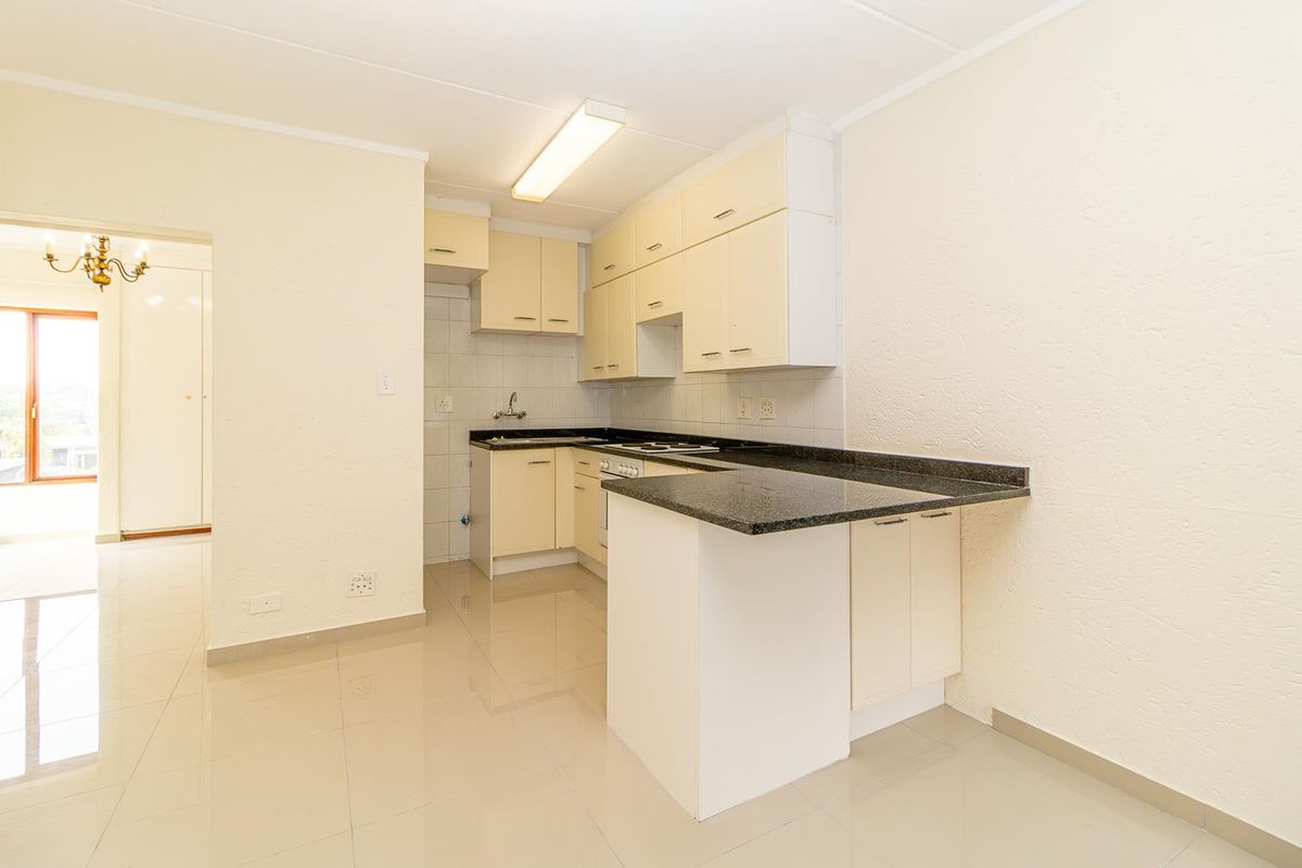 A functional kitchen featuring cream-colored cabinetry, dark granite countertops, an electric hob, and an under-counter oven, finished with neutral floor tiles.