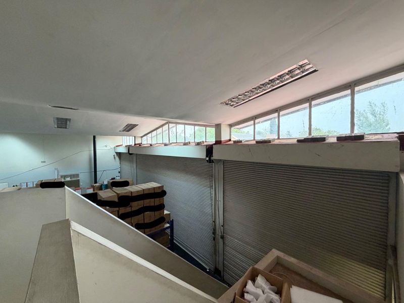 A spacious industrial utility area featuring high ceilings, clerestory windows for natural light, and large roller shutter doors, suitable for storage or workshop use.