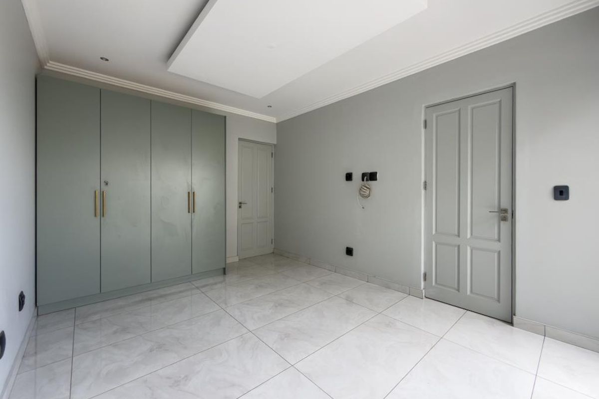 A bright, modern bedroom featuring built-in sage green cabinetry, neutral grey walls, and polished marble-look floor tiles.