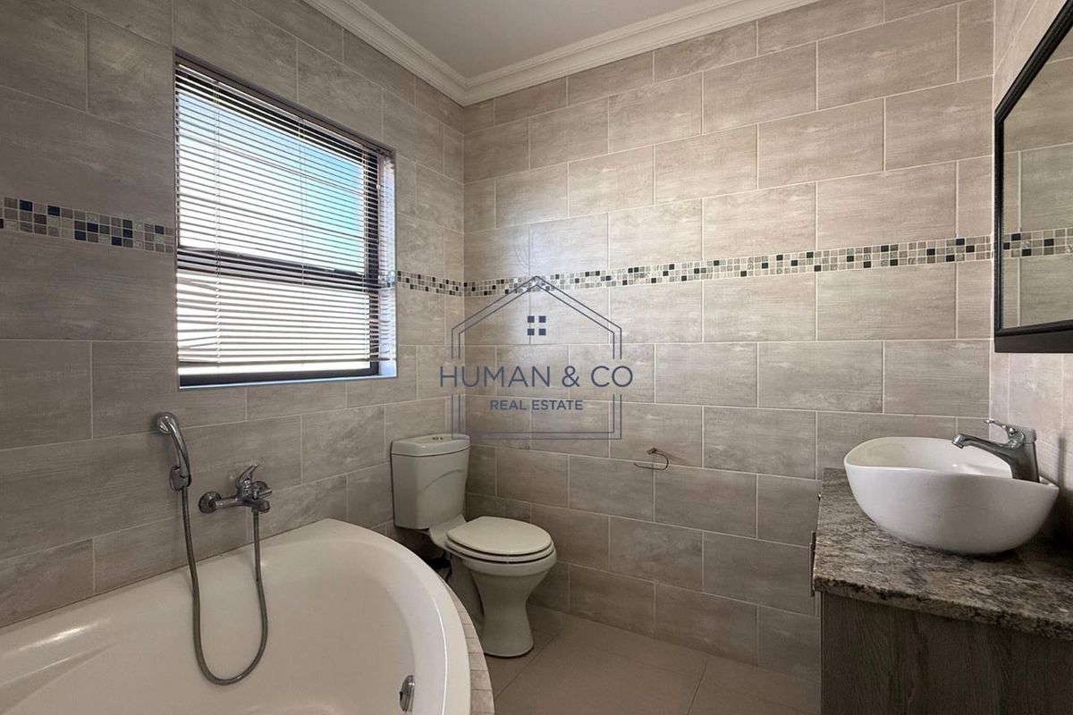 Modern bathroom featuring a built-in bathtub, a vessel sink on a stone vanity, and neutral wall tiling with a decorative mosaic accent strip.