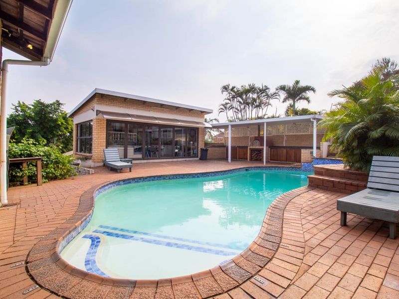 Outdoor pool area featuring a swimming pool, brick paving, and a covered patio with a built-in braai, ideal for outdoor entertaining.