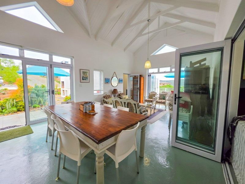 Spacious open-plan living and dining area featuring a high vaulted ceiling with exposed rafters, skylights, and large glass doors opening to the garden.