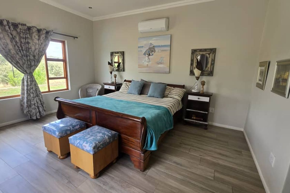 Spacious bedroom featuring wood-look tile flooring, a wall-mounted air conditioning unit, and large windows providing natural light and scenic views.