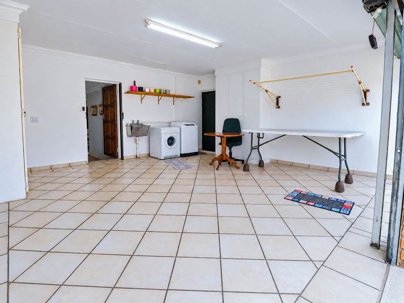 Spacious garage featuring tiled flooring, built-in storage cupboards, a utility sink, and a wall-mounted drying rack, offering versatile space for parking or laundry.