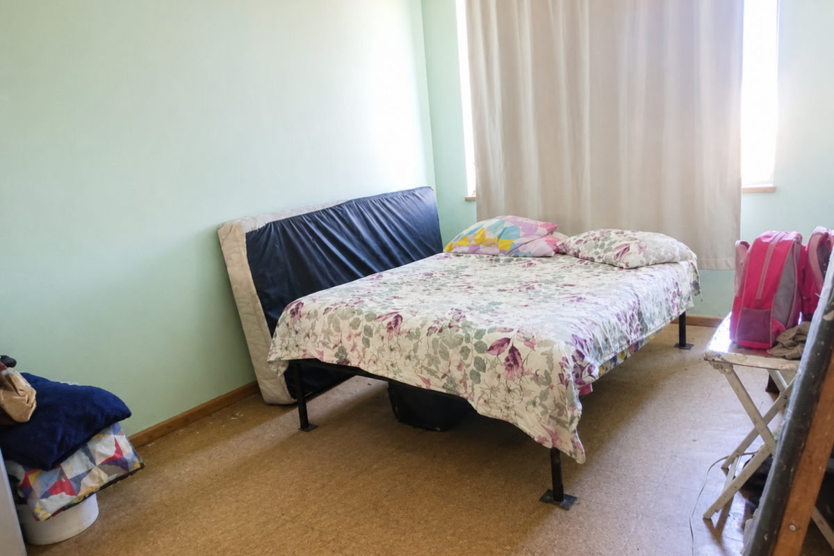 A bedroom featuring light green walls and vinyl flooring, with a window providing natural light.