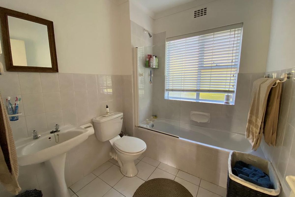 A functional bathroom featuring a pedestal basin, toilet, and a combined bathtub with a shower overhead and glass screen.