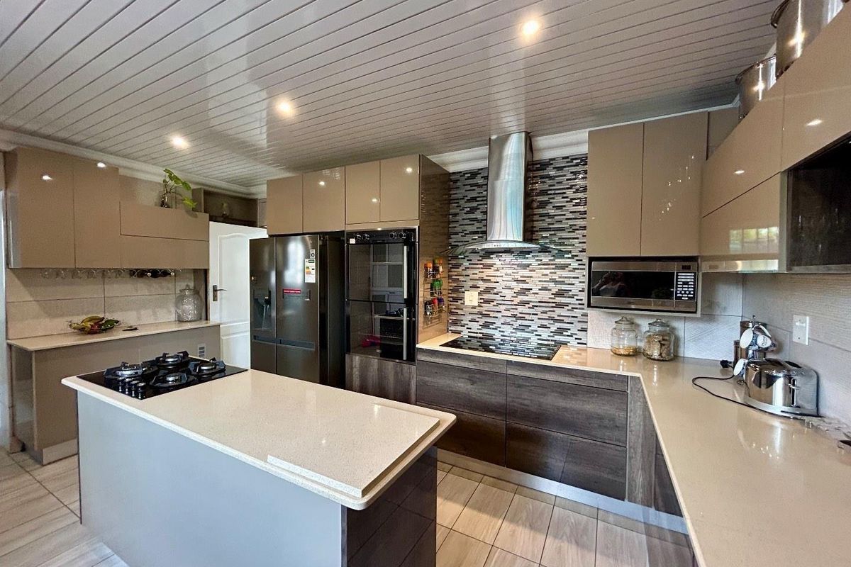Modern kitchen featuring high-gloss cabinetry, stone countertops, a central island with a gas hob, built-in oven, and a mosaic tile backsplash.
