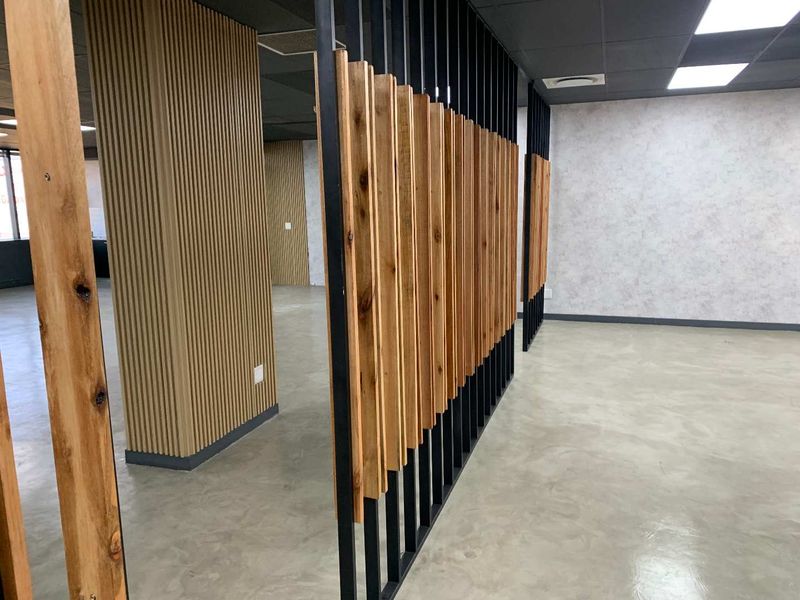 Modern open-plan office space featuring polished concrete floors, contemporary timber slat room dividers, and high-quality wall cladding with recessed ceiling lighting.