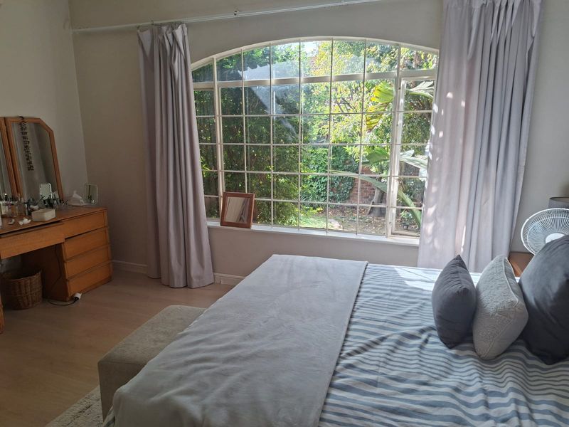 A bright bedroom featuring a large arched window with garden views and light-toned laminate flooring.