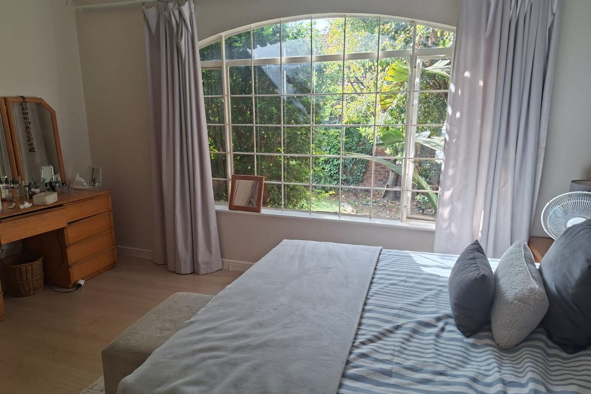 A bright bedroom featuring a large arched window with garden views and light-toned laminate flooring.