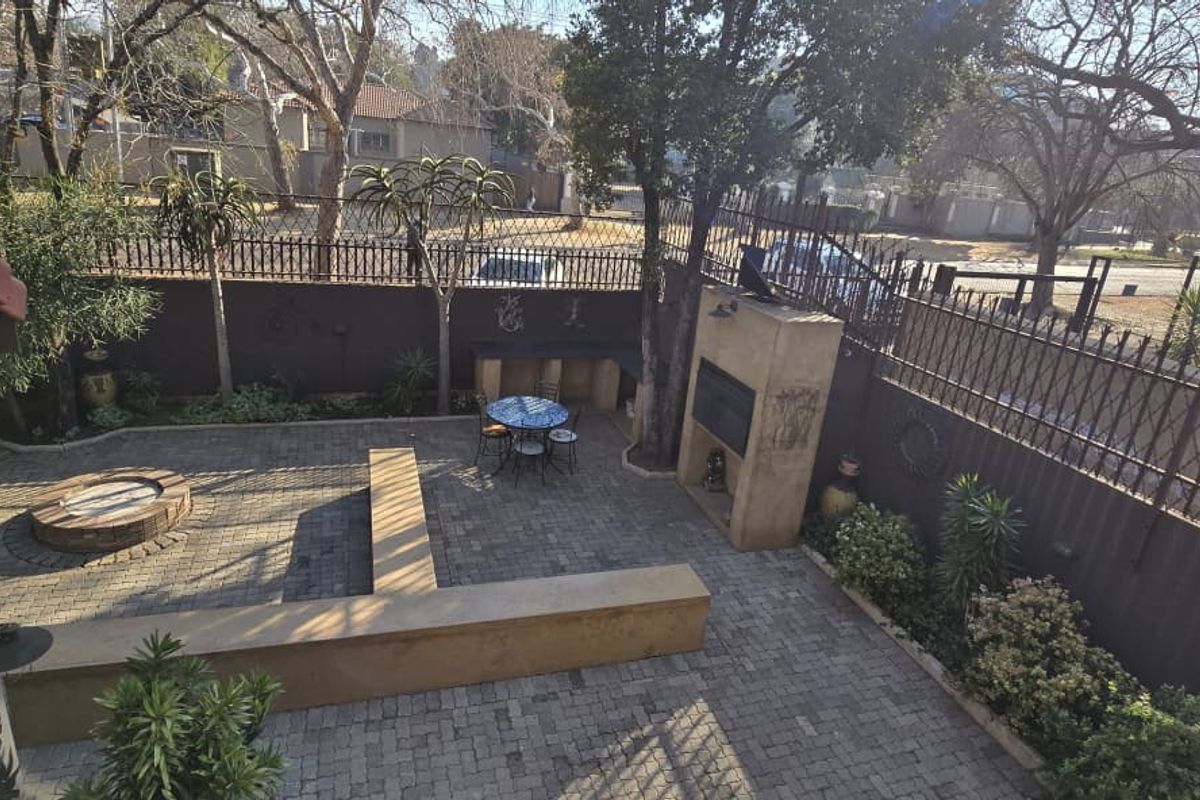 A paved rear courtyard featuring a built-in braai, a raised circular fire pit, and integrated concrete seating, enclosed by perimeter fencing.