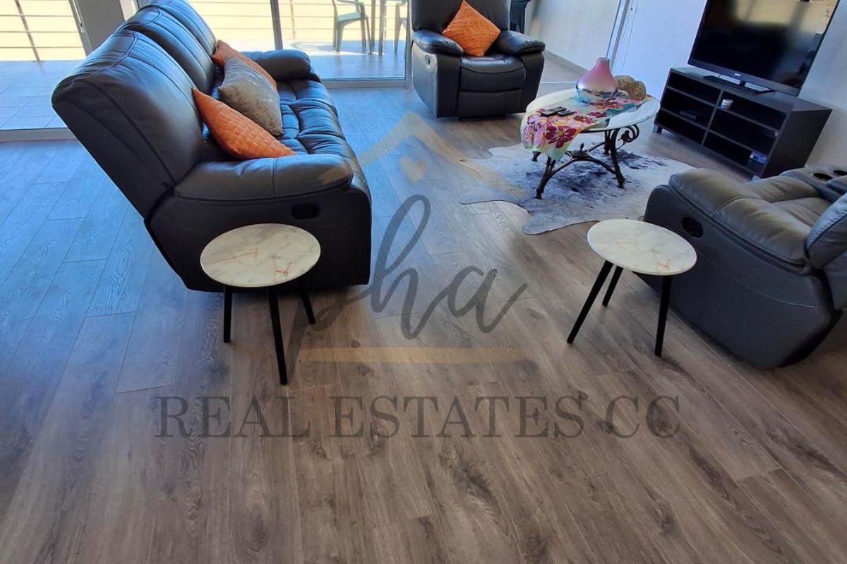 Spacious living area featuring modern wood-look flooring and large sliding glass doors that open onto a balcony with expansive ocean views.
