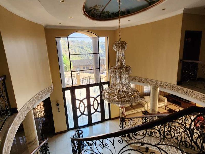 Grand entrance foyer featuring a sweeping curved staircase with ornate wrought iron balustrades, a crystal chandelier, and a decorative ceiling mural.
