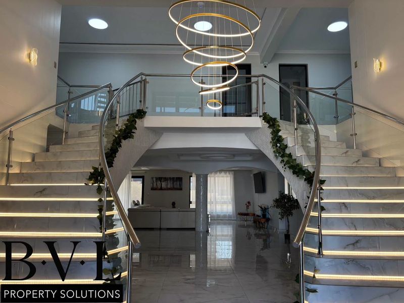 Grand entrance hall featuring a dual marble staircase with glass balustrades, integrated LED lighting, and a contemporary feature chandelier.