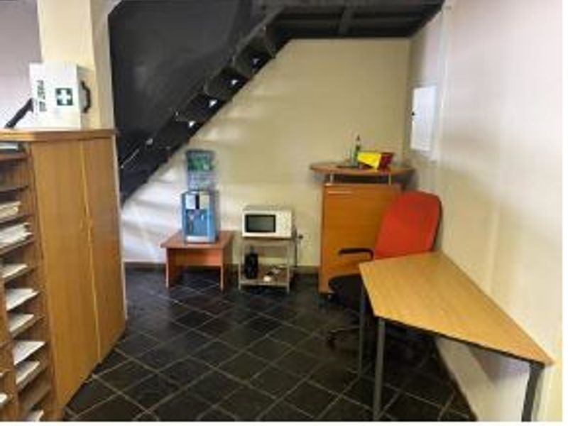 A functional office space featuring tiled flooring and an integrated staircase, providing a practical work environment with built-in storage and utility access.