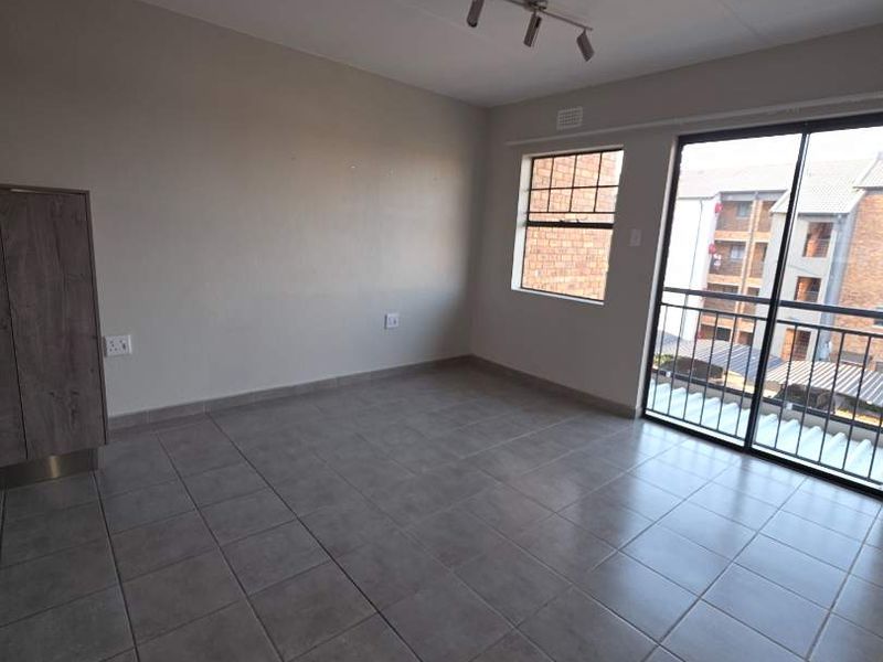 An empty, open-plan living area featuring neutral tiled flooring, a built-in cupboard, and a sliding glass door leading to a balcony.