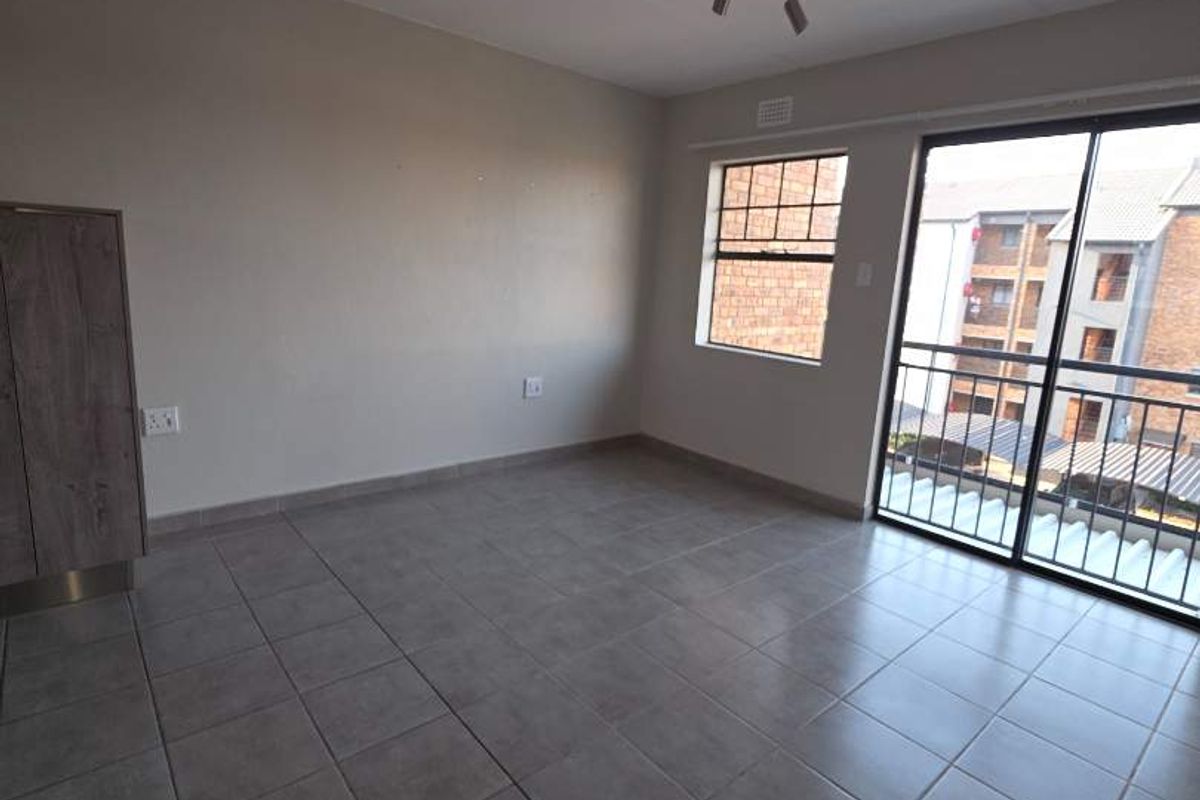 An empty, open-plan living area featuring neutral tiled flooring, a built-in cupboard, and a sliding glass door leading to a balcony.