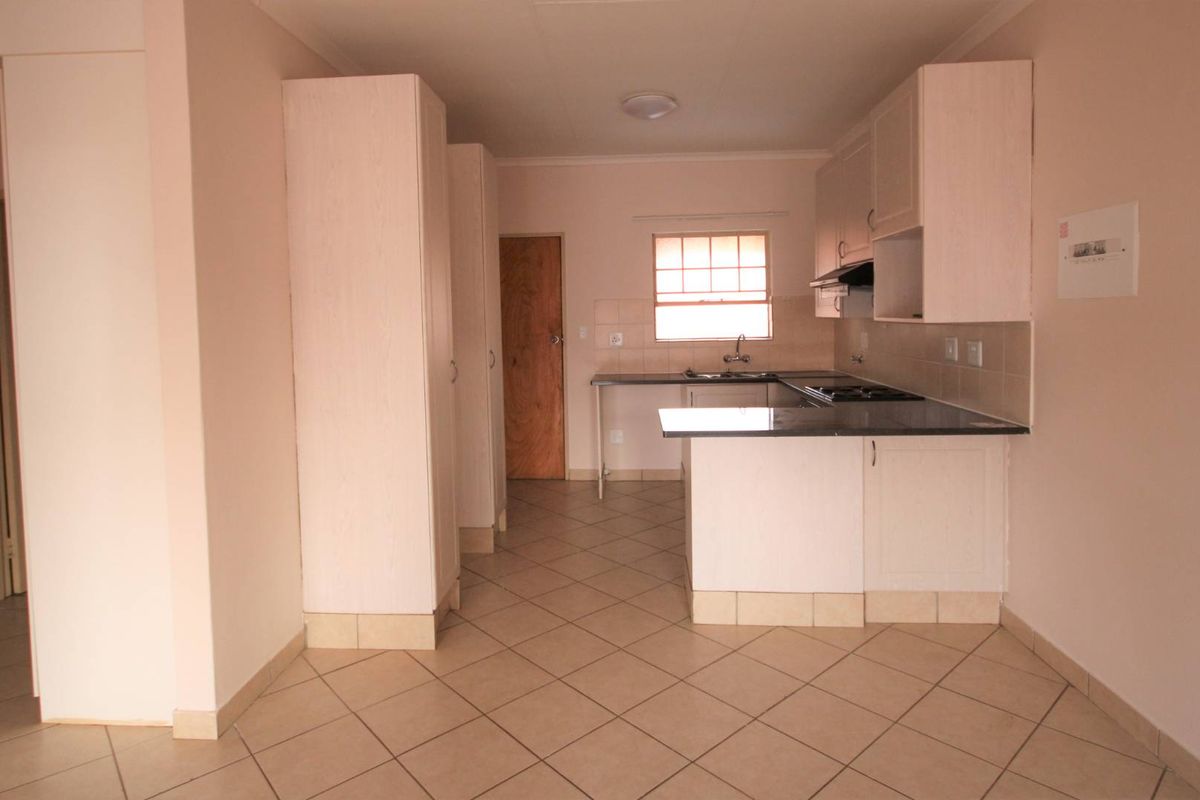 A functional kitchen featuring built-in cabinetry, laminate countertops, a hob with extractor fan, and tiled flooring in an open-plan layout.