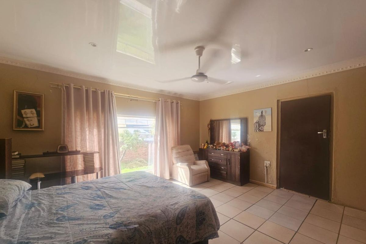 Spacious bedroom featuring a high-gloss ceiling, ceiling fan, and tiled flooring with direct access to the garden through large windows.