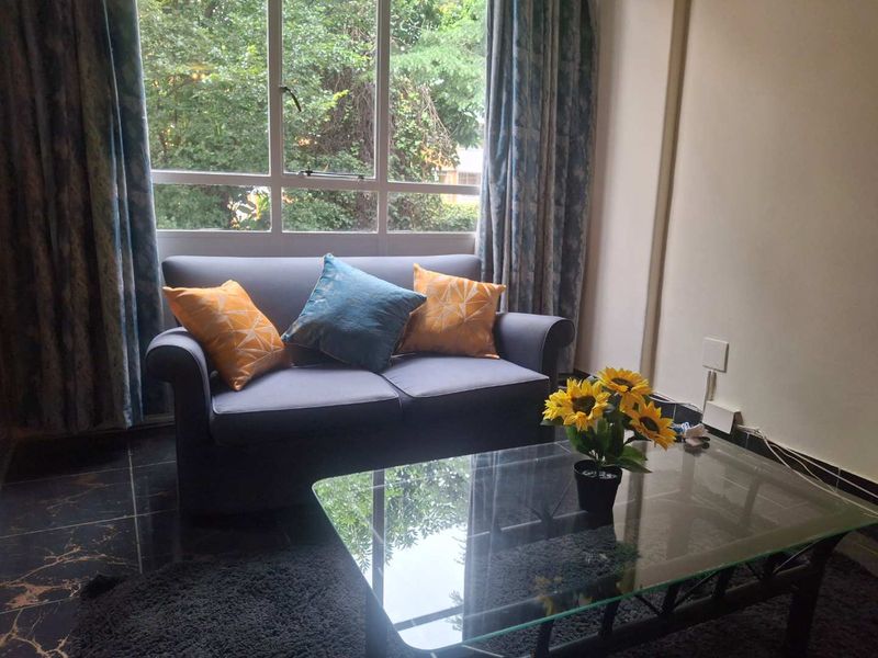 A cozy living room area featuring large windows that provide natural light and views of the surrounding greenery.