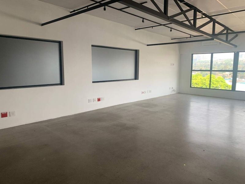 A spacious, modern open-plan office featuring polished concrete floors, exposed industrial steel trusses, and large windows providing ample natural light and views.