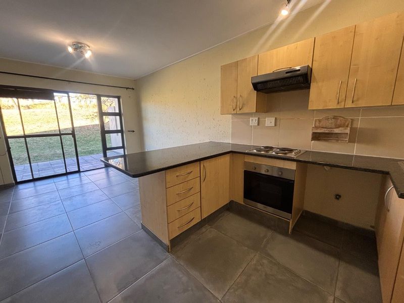 Open-plan kitchen and living area featuring light wood cabinetry, granite countertops, built-in appliances, and direct access to an outdoor patio through sliding glass doors.