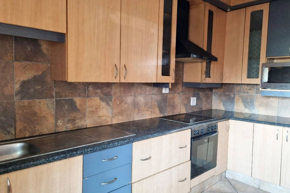 A functional kitchen featuring wood-finish cabinetry, granite countertops, a built-in oven, hob, and extractor fan with a tiled backsplash.