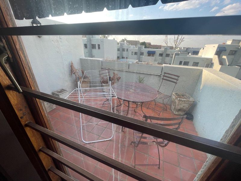 A compact balcony featuring terracotta tiling and a concrete parapet wall, viewed through a security gate.