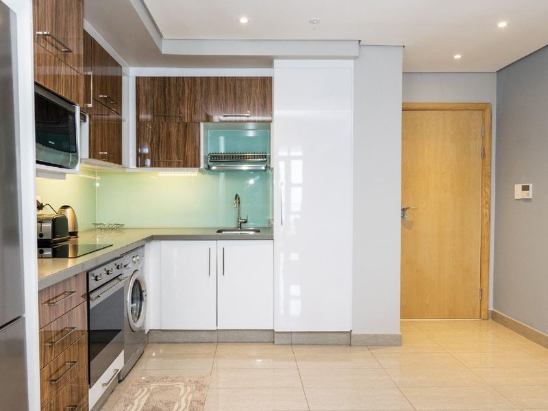 Modern kitchen featuring high-gloss and wood-grain cabinetry, stone countertops, glass splashback, and integrated appliances including an oven, hob, and washing machine.