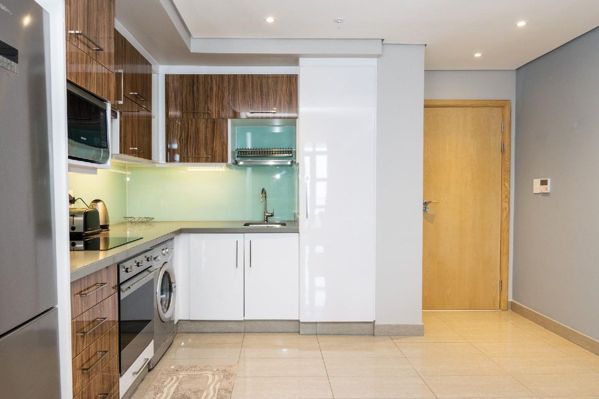 Modern kitchen featuring high-gloss and wood-grain cabinetry, stone countertops, glass splashback, and integrated appliances including an oven, hob, and washing machine.