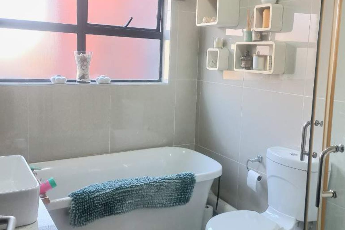 A modern bathroom featuring a freestanding bathtub, a separate glass-enclosed shower, a vanity basin, and a toilet with neutral wall and floor tiling.
