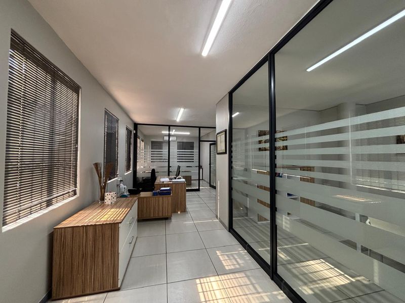 Modern office space featuring glass partition walls, tiled flooring, and natural light through venetian blinds, creating a professional and open work environment.