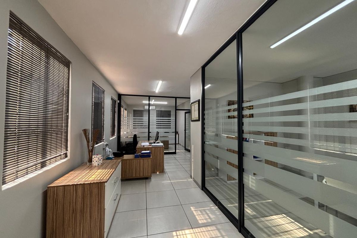 Modern office space featuring glass partition walls, tiled flooring, and natural light through venetian blinds, creating a professional and open work environment.