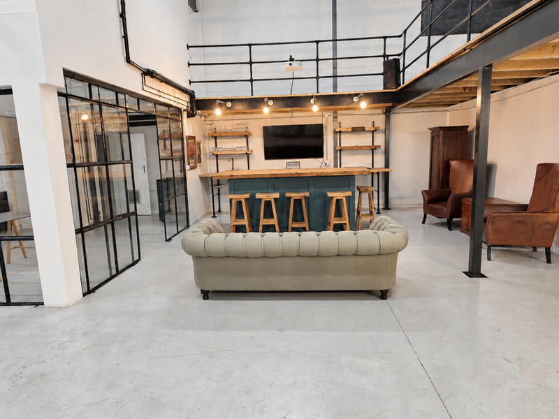 Spacious industrial open-plan area featuring a mezzanine level, steel-framed glass partitions, polished concrete floors, and a built-in bar counter.