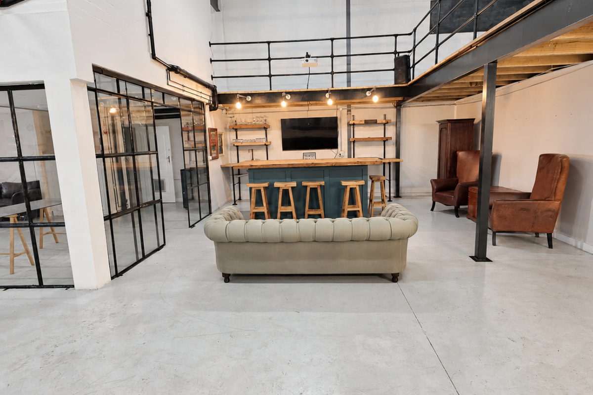 Spacious industrial open-plan area featuring a mezzanine level, steel-framed glass partitions, polished concrete floors, and a built-in bar counter.
