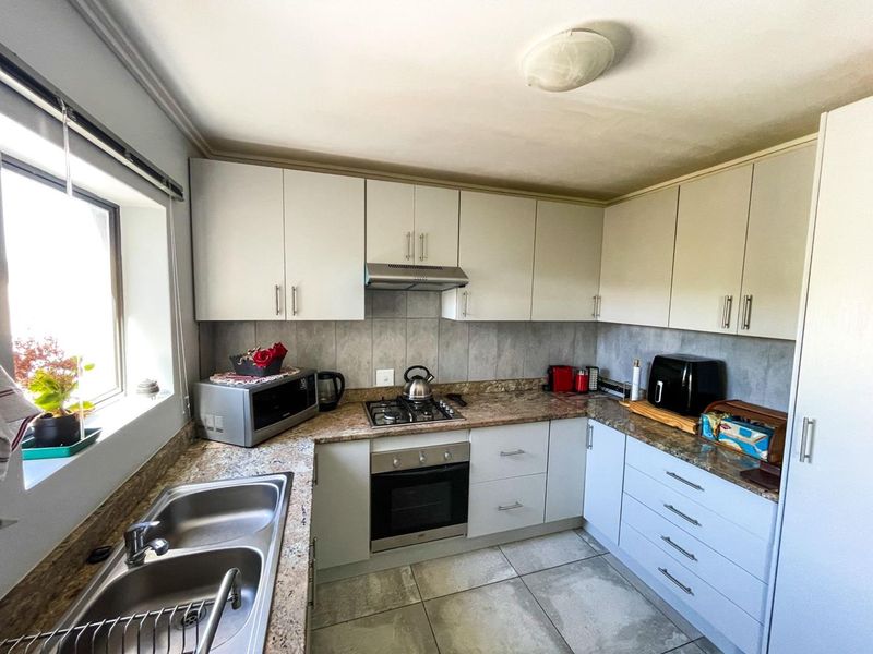 A functional kitchen featuring light-toned cabinetry, granite-look laminate countertops, a gas hob with extractor, and tiled flooring.