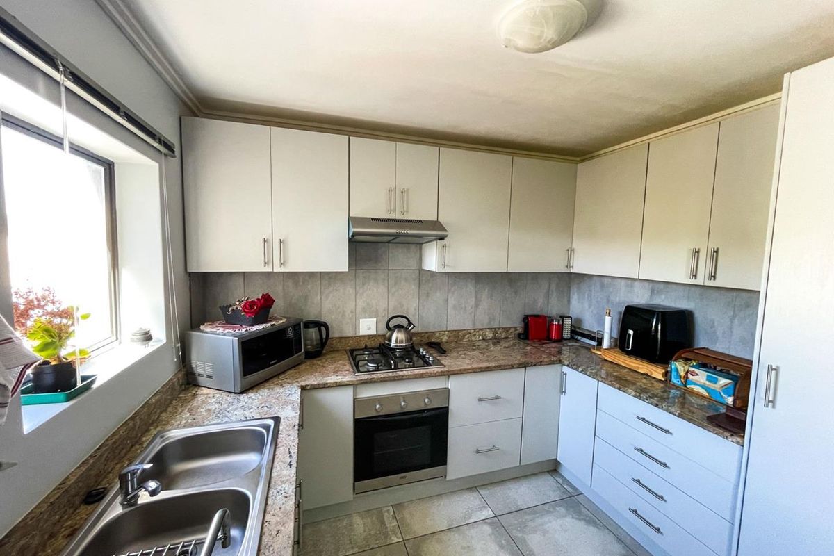 A functional kitchen featuring light-toned cabinetry, granite-look laminate countertops, a gas hob with extractor, and tiled flooring.