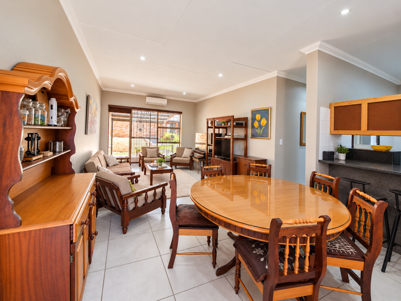 Spacious open-plan living and dining area featuring tiled floors, recessed lighting, and a breakfast bar, seamlessly connecting to the outdoor patio space.