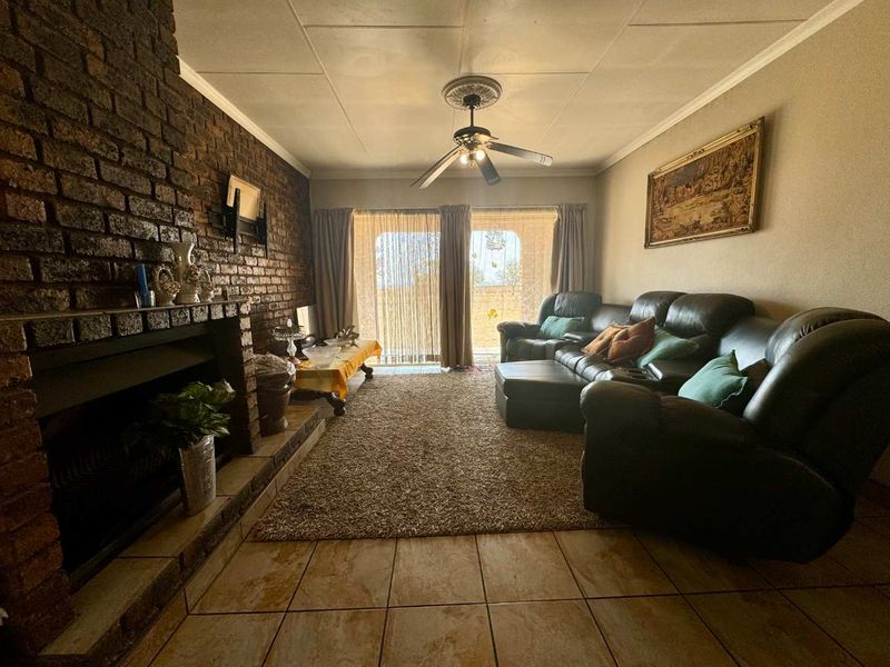 A cozy living room featuring a prominent brick fireplace, tiled flooring, and a ceiling fan, with direct access to the outdoors via sliding glass doors.